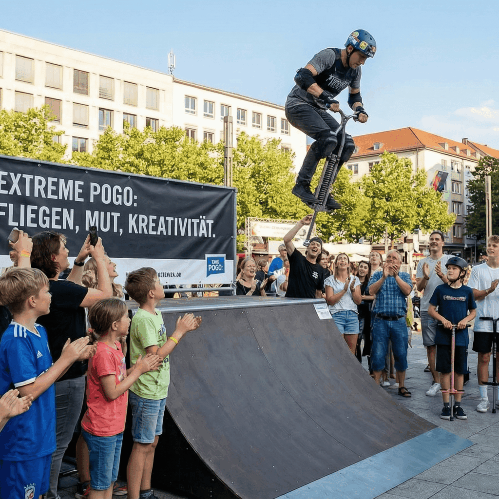 Person springt mit Pogo Stick auf einer Rampe mit vielen Personen die ihn anfeuern.