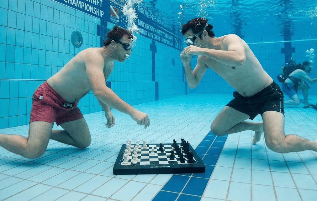 2 Schwimmer tauchen in einem Pool und spielen Unterwasser Schach auf dem Boden